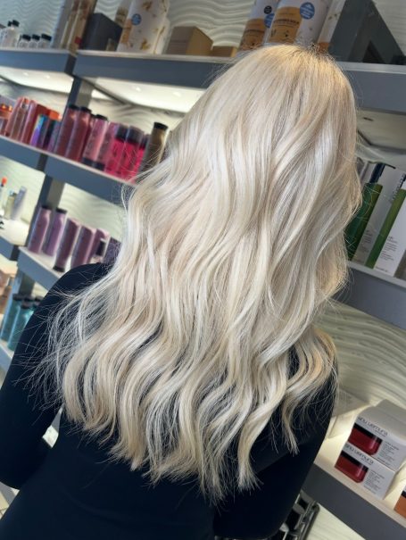 Long wavy blonde hair viewed from behind, set against a display of hair products.