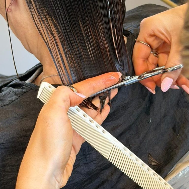 A person's hand holding a comb beside scissors cutting long hair.