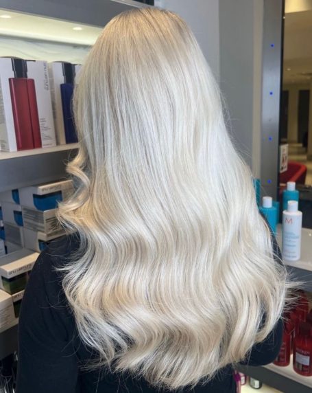 Long, wavy platinum blonde hair viewed from the back, displayed against a salon backdrop.